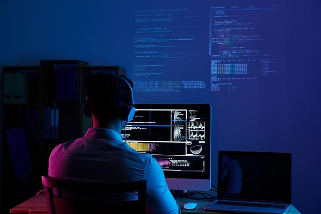 Desarrollador trabajando frente a una computadora con código en pantalla en un ambiente oscuro.